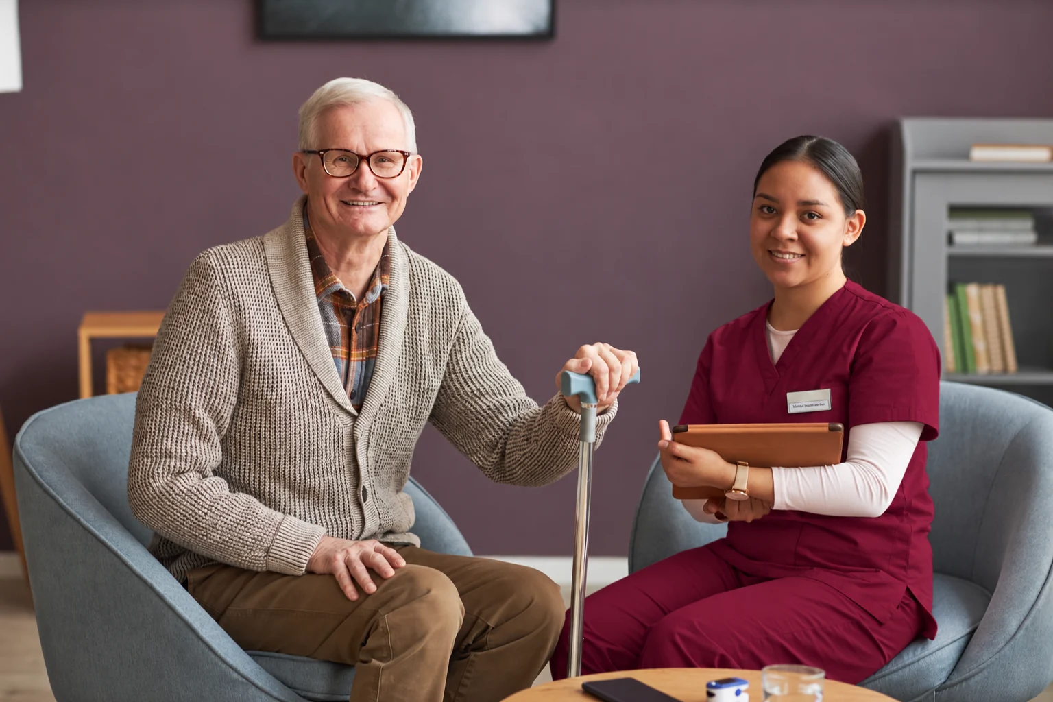 Care professional in a matching burgundy uniform supporting a patient.