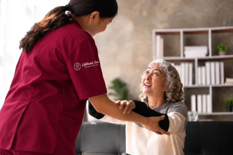 LifeTouch Care carer in burgundy scrubs with an embroidered sleeve logo