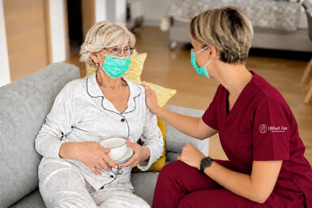 LifeTouch Care carer in burgundy scrubs with an embroidered sleeve logo